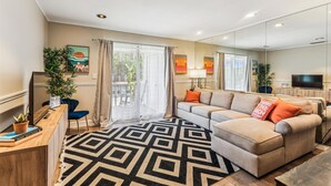 Una sala de estar moderna con un sofá, una mesa de centro y un televisor. Hay cortinas, una planta y una alfombra.