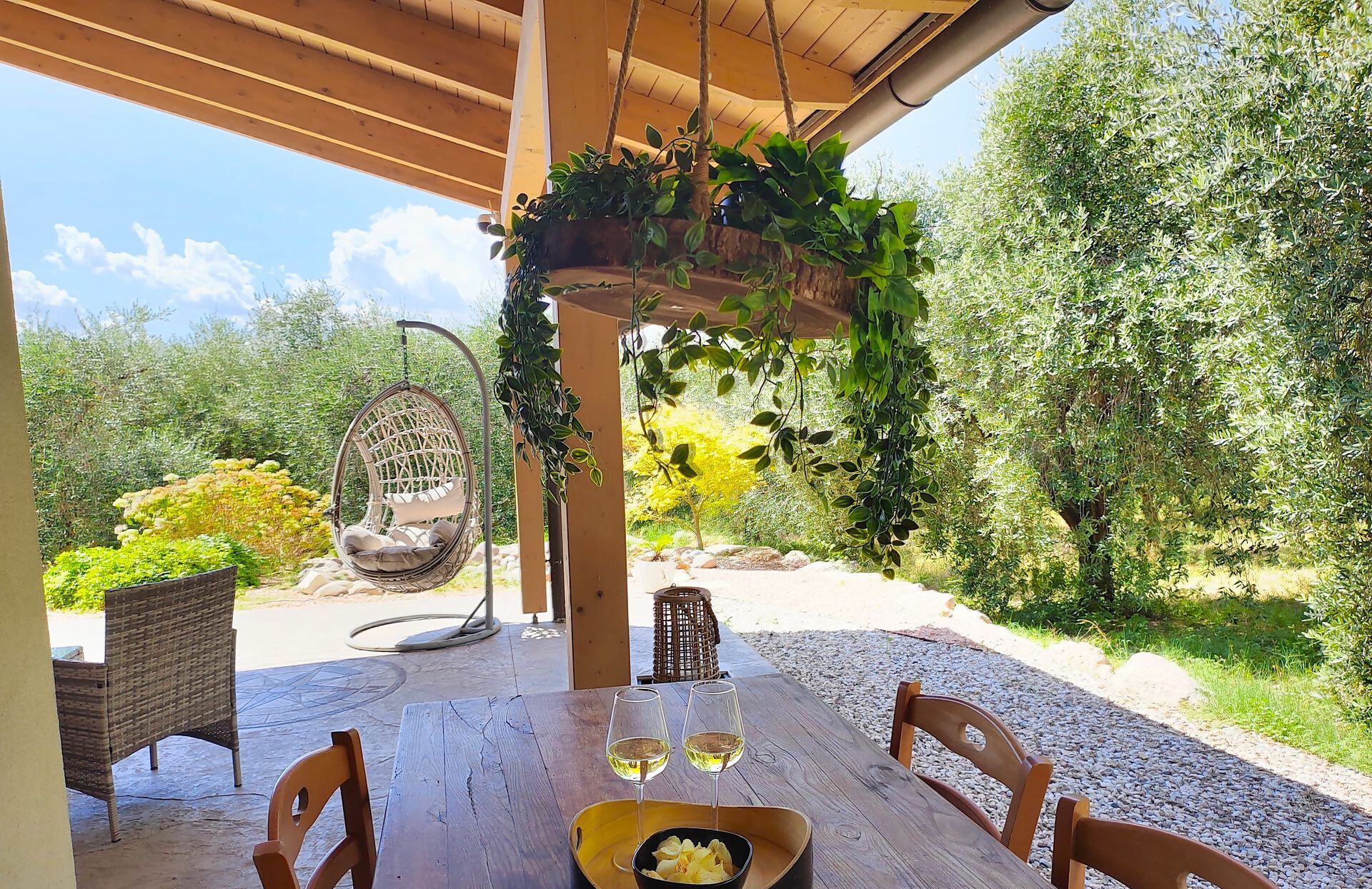 Un'area pranzo all'aperto con tavolo in legno, sedie in vimini, una sedia a dondolo e una ciotola di cibo.
