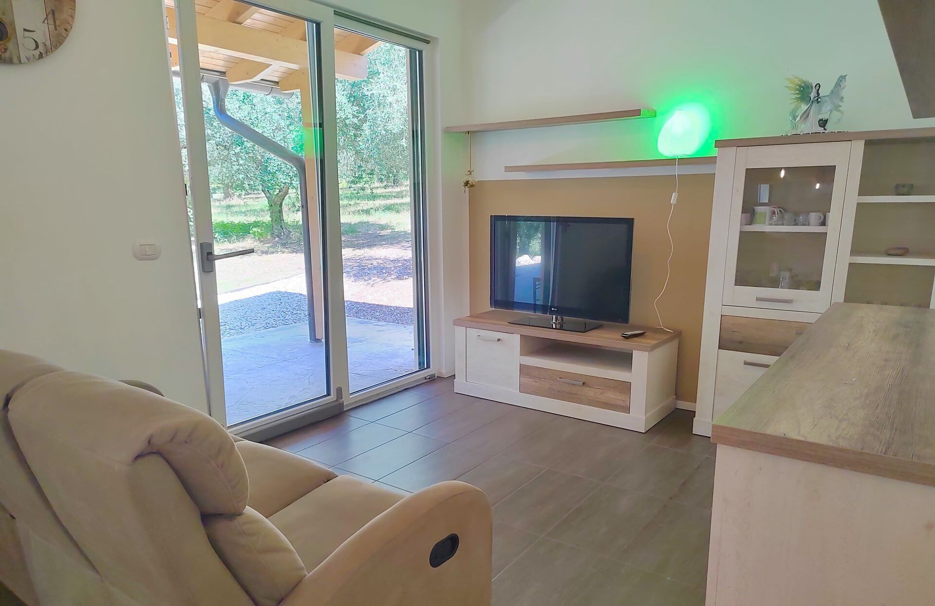Un salon comprenant un canapé, un téléviseur posé sur un meuble en bois, un buffet avec des portes en verre et une porte-fenêtre coulissante donnant sur l’extérieur.