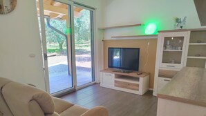 Ein Wohnzimmer mit einer Couch, einem Fernseher auf einem Holzschrank, einer Vitrine und einer Glastür zum Garten.