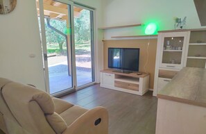 A living room with a sofa, a TV on a wooden stand, a cabinet with glass doors, and a sliding glass door leading outside.