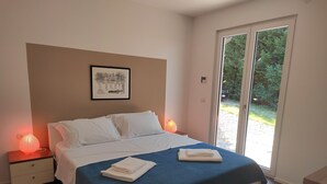 Une chambre avec un lit, une table de chevet, un tableau encadré au mur et une vue sur la verdure par une porte coulissante.