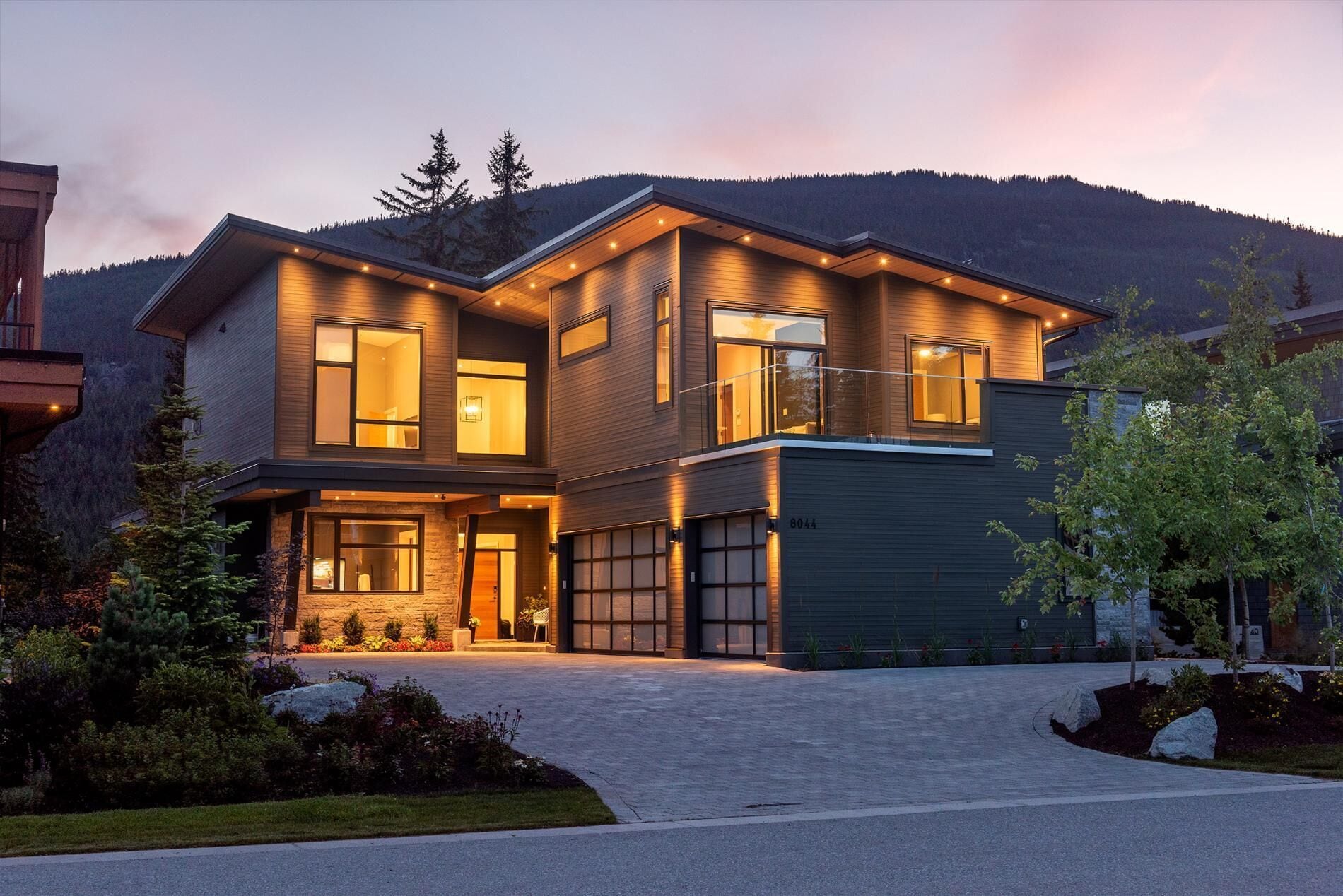 A modern two-story house with a garage, large windows, and a well-lit entrance.