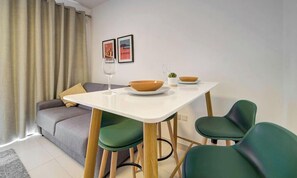 Un comedor con una mesa blanca, sillas verdes y un sofá al fondo.