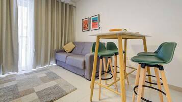 Una sala de estar moderna con un sofá, una mesa de comedor con sillas y un ventanal con cortinas.