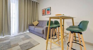 A modern living room with a sofa, a dining table with chairs, and a large window with curtains.