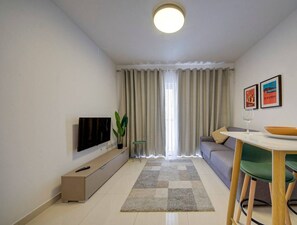 A modern living room with a flat-screen TV, a sofa, a dining table with chairs, and a large window with curtains. - Beautiful, central Gzira 1BR home w/Wifi & AC (Gżira)