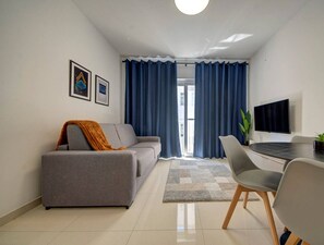 A modern living room with a grey sofa, a coffee table, and a TV. There are blue curtains and a plant on the table.