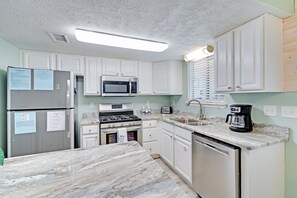 A kitchen with white cabinets, a stainless steel refrigerator, a microwave, a stove, a dishwasher, and a coffee maker.