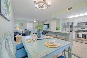 A dining area with a table set for four, a chandelier, and a kitchen in the background.