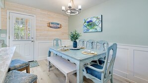 Un espace repas avec une porte en bois, un lustre, un panneau d’accueil et un tableau accroché au mur.