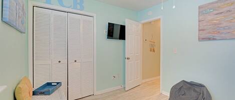 Una habitación con una puerta cerrada, un televisor en la pared, un sillón informal y una obra de arte colgada.