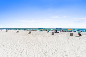 A beach with white sand, umbrellas, and people.