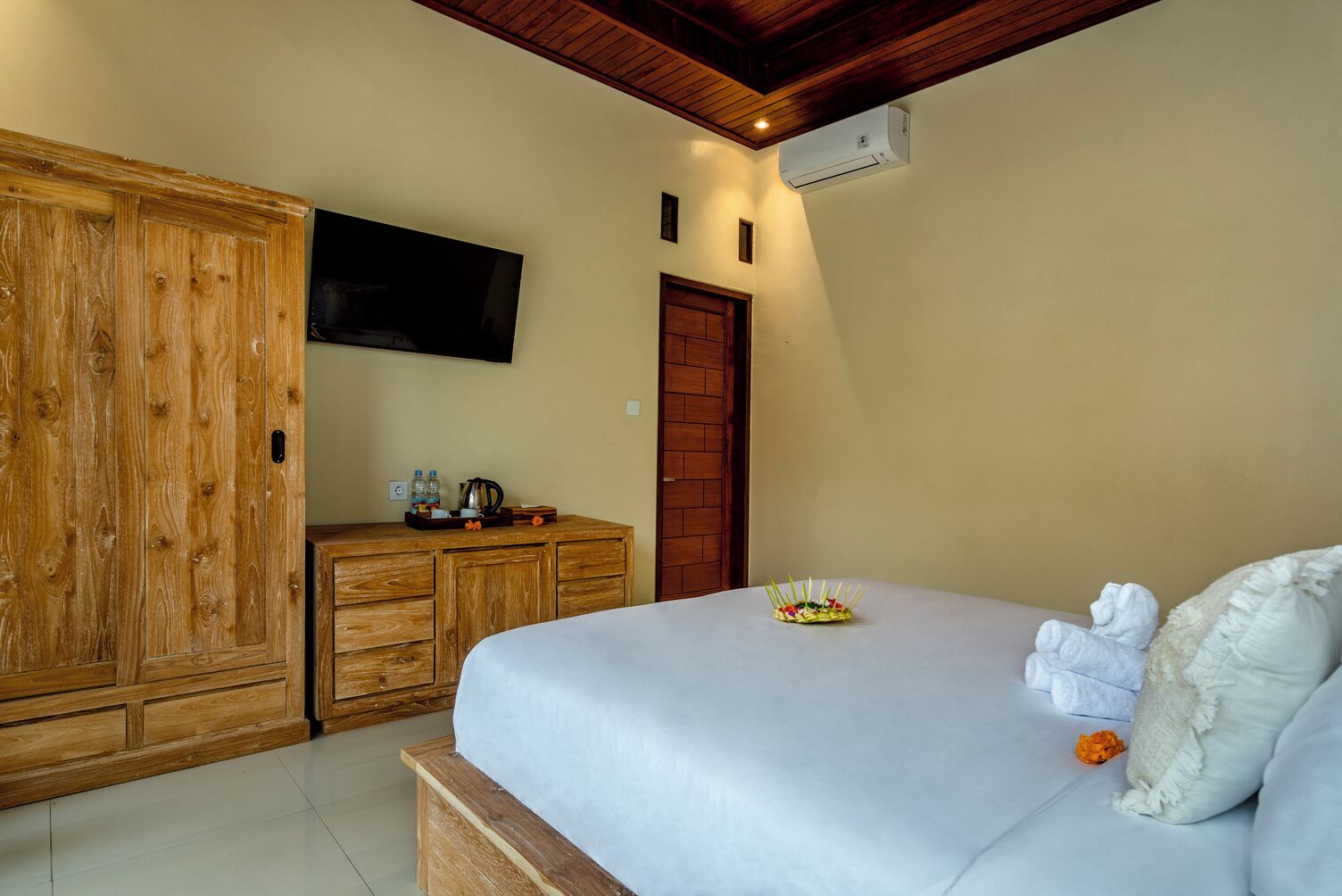 A bedroom with a bed, wooden wardrobe, a television mounted on the wall, and an air conditioning unit.