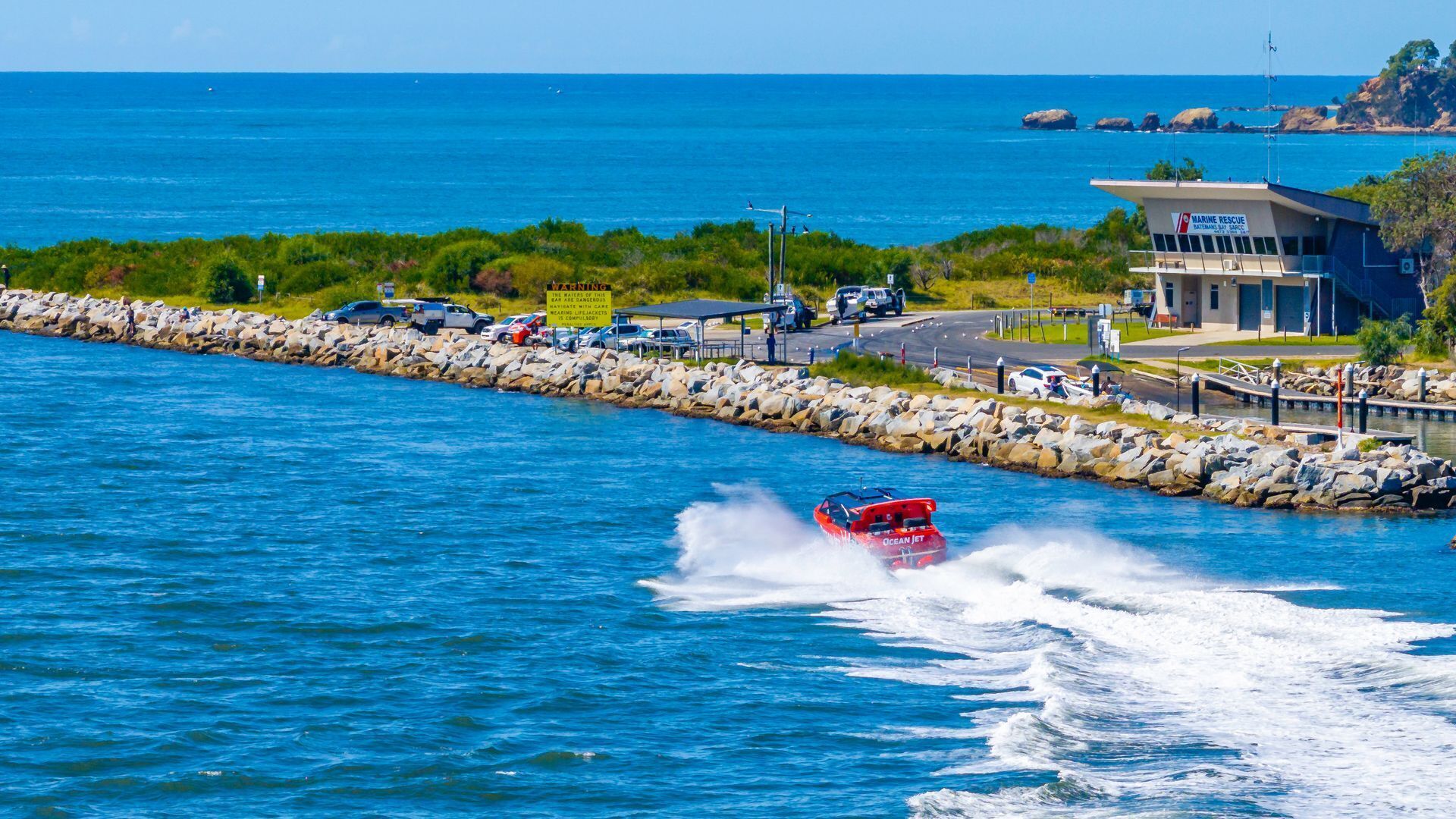 Una zona costiera con un jet ski, un edificio per il soccorso marittimo e un molo roccioso.