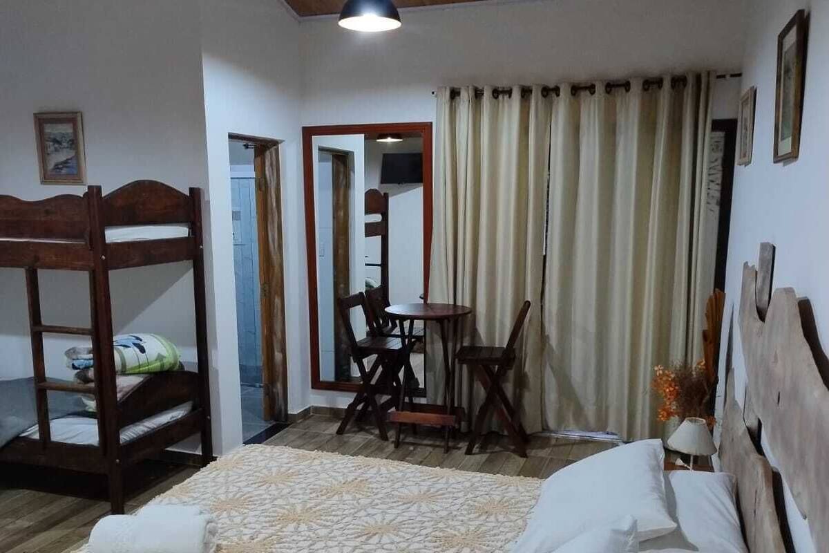 A bedroom with a bunk bed, a single bed with patterned bedding, a ceiling fan, a table with chairs, and a television in the corner.
