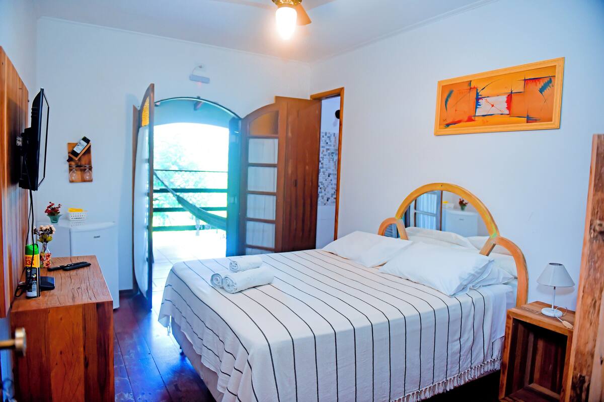 A bedroom with a bed, a wooden desk, a television, and a door leading outside.