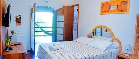 A bedroom with a bed, a wooden desk, a television, and a door leading outside.
