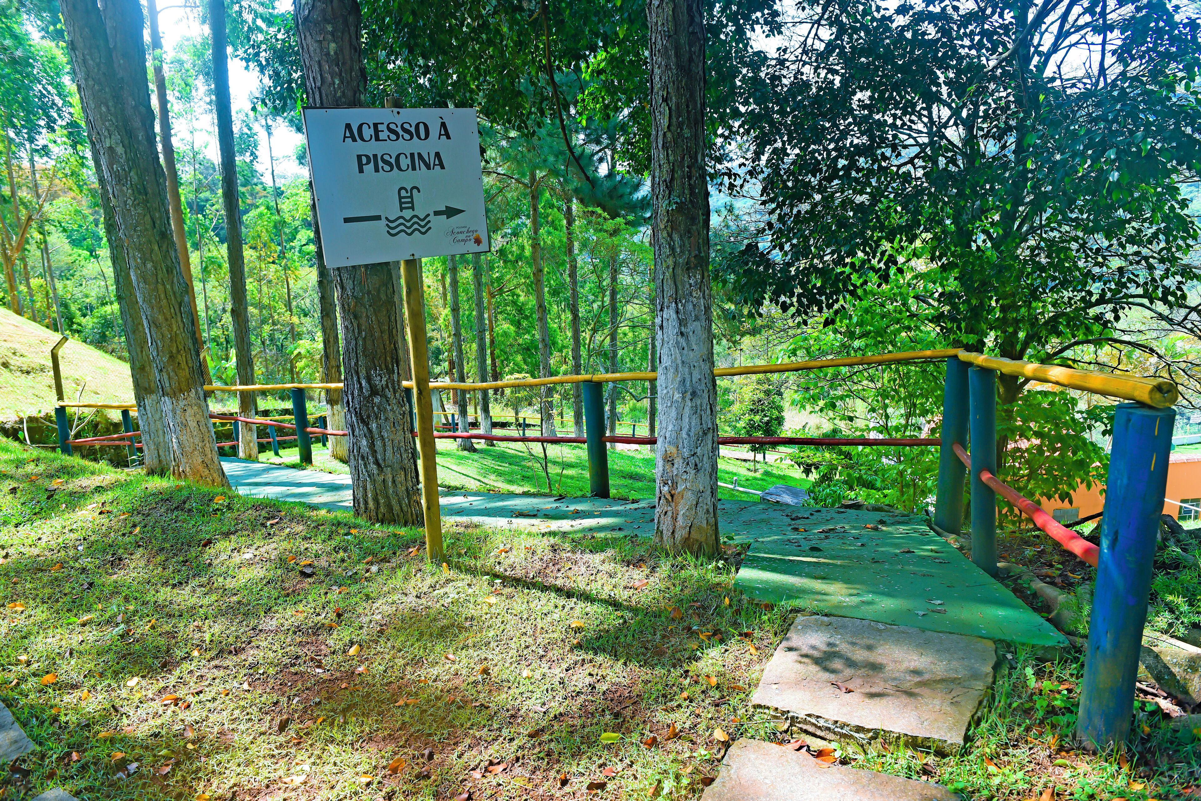 A sign indicating access to a swimming area, surrounded by trees and a playground.