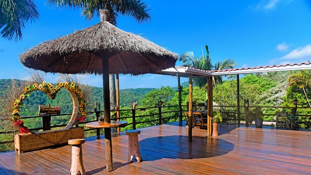 Una terraza de madera con un pabellón de techo de paja, un arreglo floral en forma de corazón y un letrero que dice "Panorama Garden".