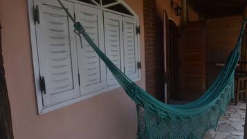 A hammock tied to a white door with a window, a brick wall, and a wooden door in the background.