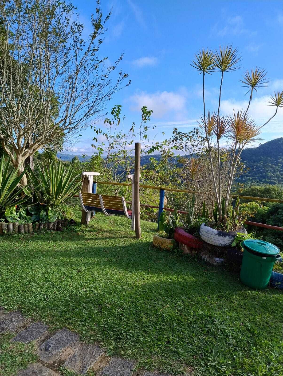 A grassy outdoor area with a wooden bench, various potted plants, and a view of distant hills.