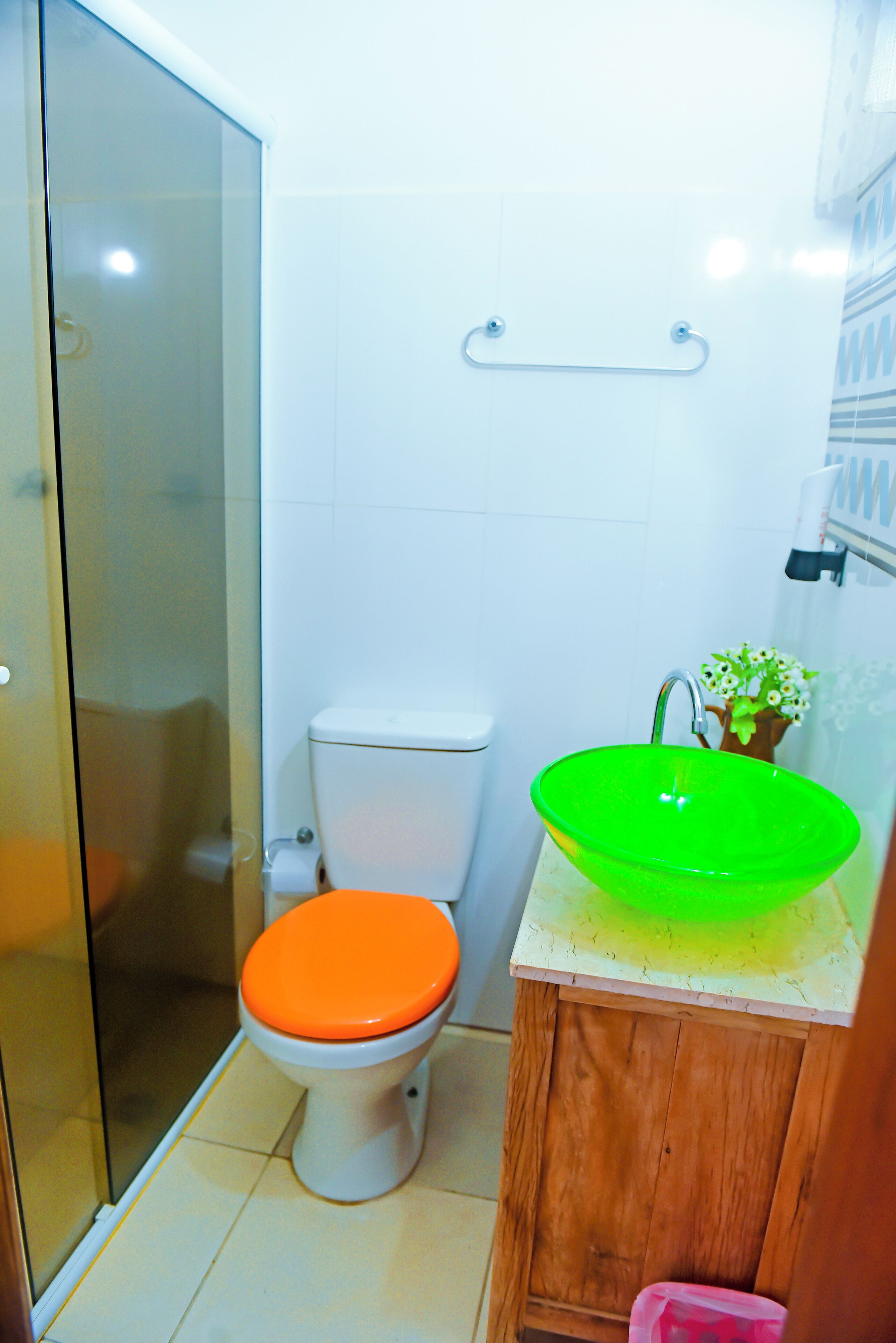 Une salle de bain avec une douche à parois de verre, des toilettes blanches avec un abattant orange et un meuble en bois avec un lavabo vert.