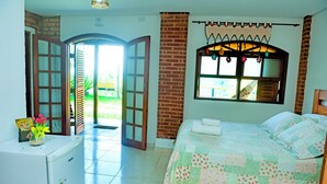 Un dormitorio con cama, un refrigerador pequeño, una ventana con cortinas y una puerta que da a un área exterior.
