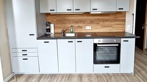 A modern kitchen with white cabinets, a stainless steel oven, and a wooden backsplash. - Jessi`s Harz Apartment (Sankt Andreasberg)