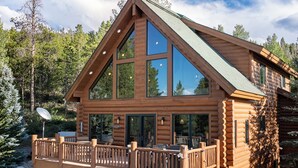Une cabane en rondins dotée d’un balcon, de grandes fenêtres et d’une antenne parabolique.