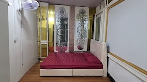 Ein kleiner, schmaler Raum mit einem Einzelbett, einem Wandventilator und dekorativen Wandverkleidungen.