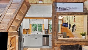A modern kitchen with white cabinets, stainless steel appliances, and a hanging pot rack. - A-Frame @ Entrance to Rainier w/ Hot Tub & WiFi (Ashford)