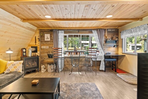 Un intérieur de chalet chaleureux avec un coin repas, des murs en bois et une vue sur l’extérieur.