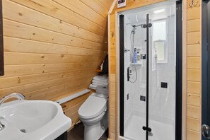 A wooden-paneled bathroom with a glass-enclosed shower, a sink, and a toilet.