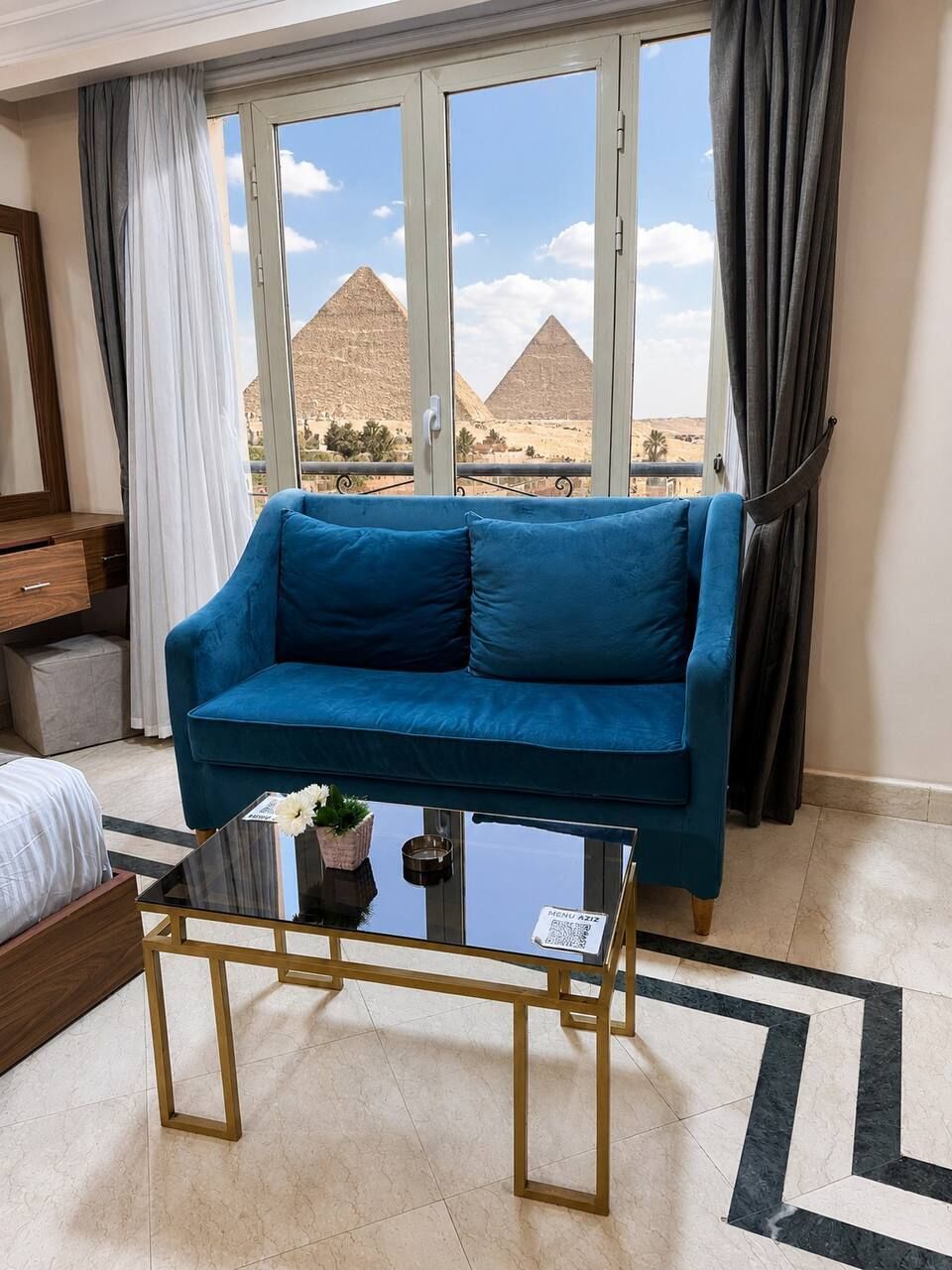 A room with a blue sofa, a glass coffee table, and a view of pyramids.