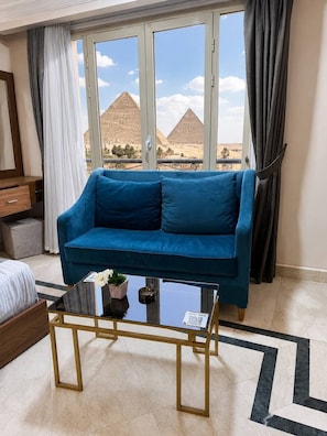 A room with a blue sofa, a glass coffee table, and a view of pyramids. -  Aziz Egypt Pyramids View (Giza)