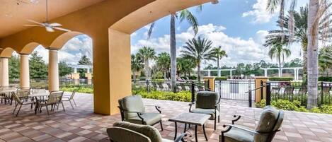 A covered outdoor seating area with chairs and tables, palm trees, and a view of a parking area.