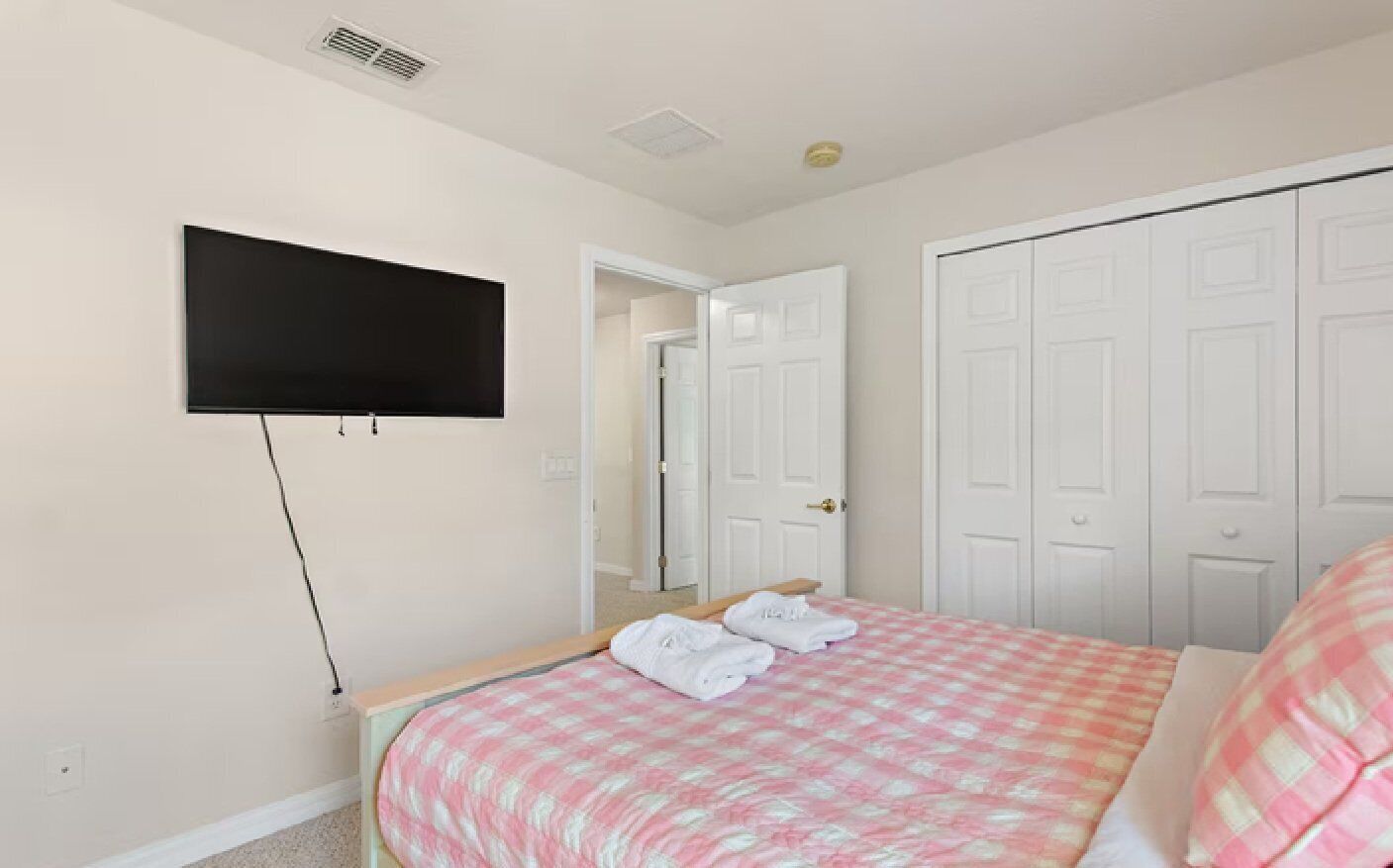 Une chambre à coucher avec un lit, un téléviseur à écran plat fixé au mur et un placard aux portes blanches.