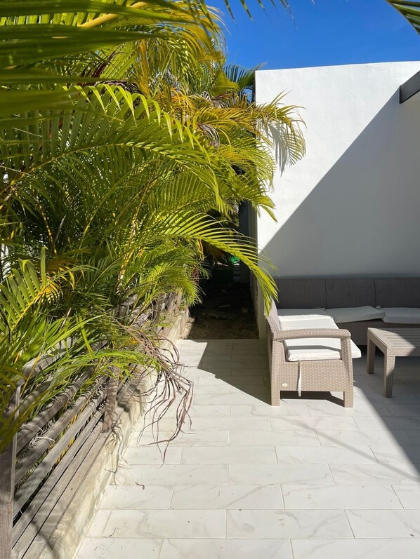 Eine Terrasse mit weißer Mauer, Holzlattenzaun und einer Sitzecke mit zwei Stühlen und einem Tisch.
