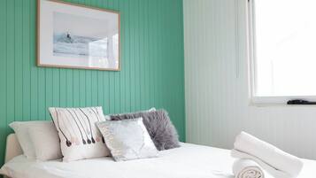A neatly made bed with white linens, a framed picture on the wall, and a window with blinds.