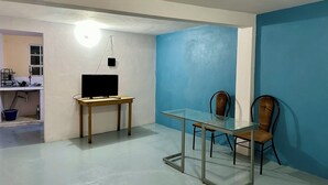 A room with a glass dining table, two chairs, a TV on a wooden stand, and a blue wall.