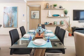 Een eethoek met een glazen tafel, zwarte stoelen en diverse decoratieve objecten op planken.