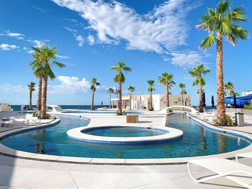 A pool area with palm trees, lounge chairs, and a clear view of the ocean.