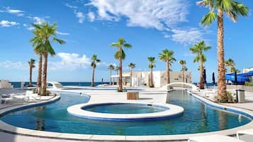 Un espace piscine agrémenté de palmiers, de chaises longues et offrant une vue dégagée sur l’océan.