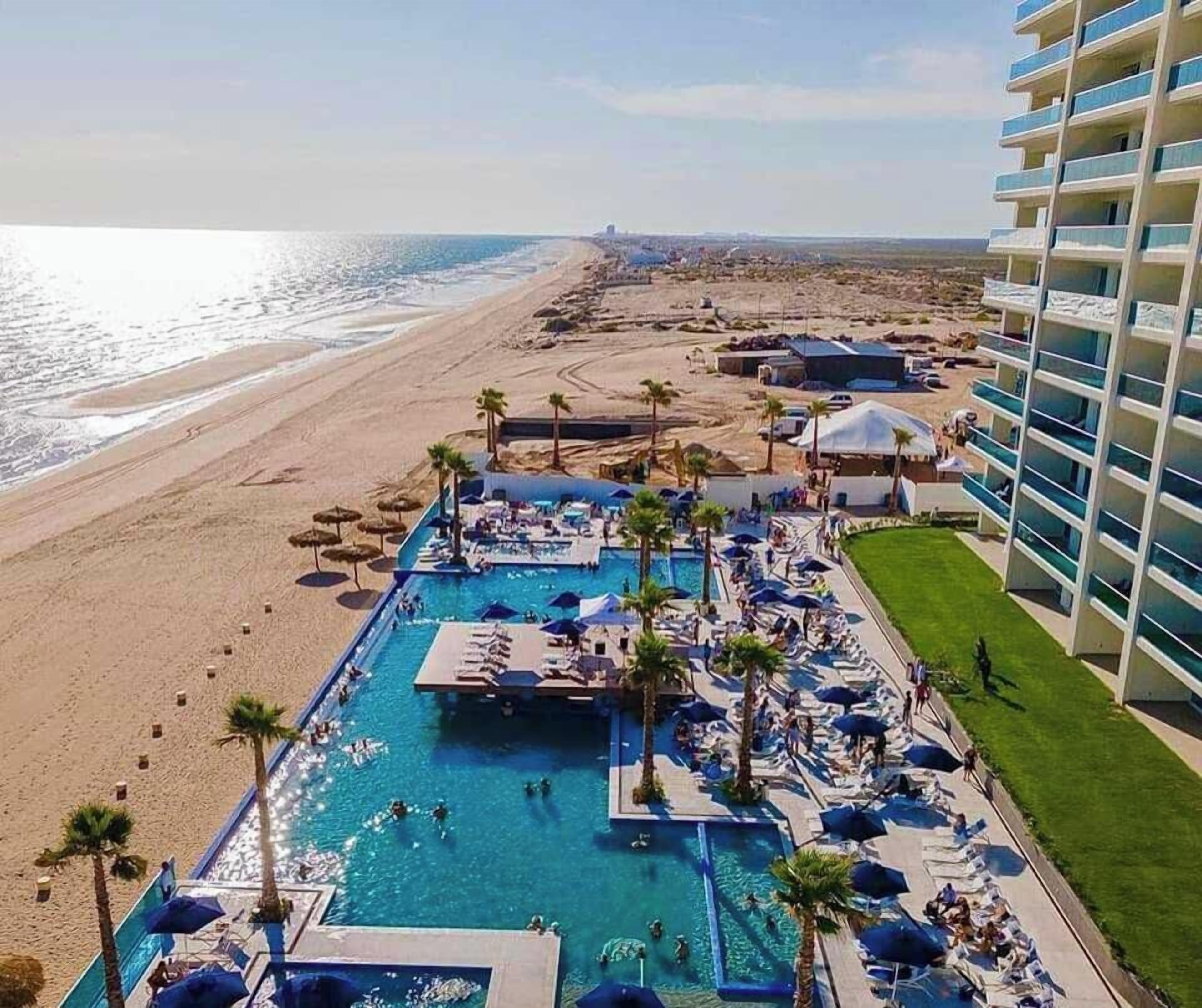 Un complexe hôtelier doté d’une grande piscine, d’un accès à la plage et d’un bâtiment avec des balcons.