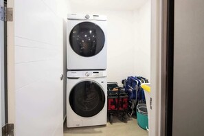 A laundry room with two stacked washing machines and a cart with cleaning supplies. - Encantame|2BR|Rooftop Pool|LazyRiver|Pickleball (Playa Encanto)