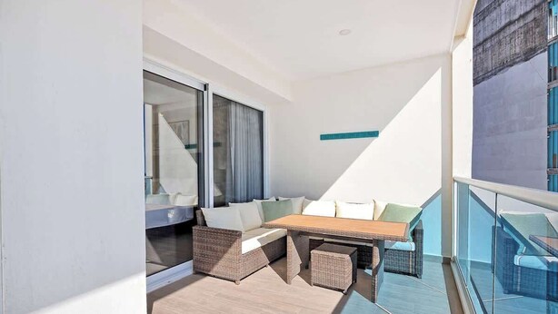 A balcony with a sofa, a table, and wicker furniture. - Encantame|2BR|Rooftop Pool|LazyRiver|Pickleball (Playa Encanto)