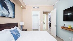 A hotel room with a bed, a TV, a painting, and a hallway leading to other rooms.