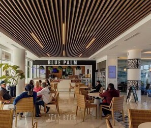 Un hall de hotel con restaurante Blue Palm, zonas de estar y un diseño de techo moderno.