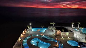 A resort with multiple swimming pools, palm trees, and a sunset view.